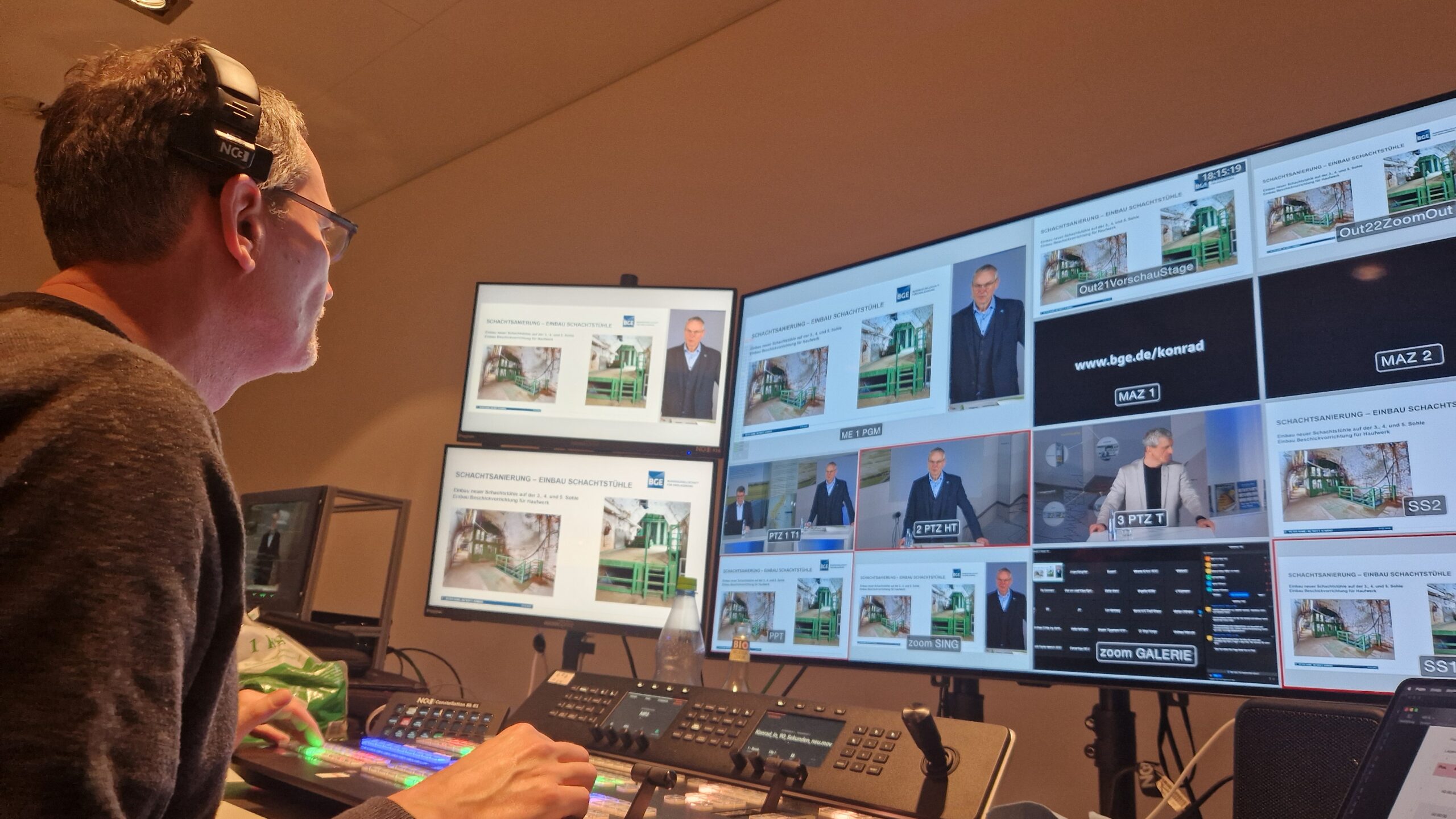 Techniker mit Headset bedient Live-Regie-Pult vor Monitorwand mit mehreren Video-Feeds und Präsentationen zu Schachtsanierung